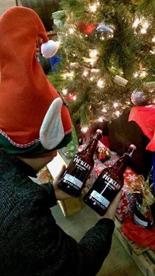 An employee dressed as an elf is photographed from behind as he sets two refillable Tappit Hen Port bottles beneath the Christmas tree.