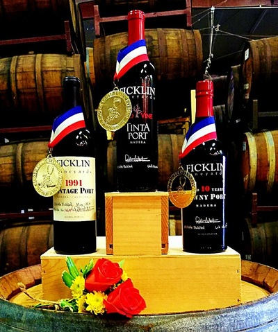 Three gold-medal winning Ficklin Ports displayed with ribbons around each bottle on a 3-level platform with flowers in front of them--like in the Olympic ceremonies:  Old Vine Tinta, Aged 10-Years Tawny, and 1996 Vintage Ports.