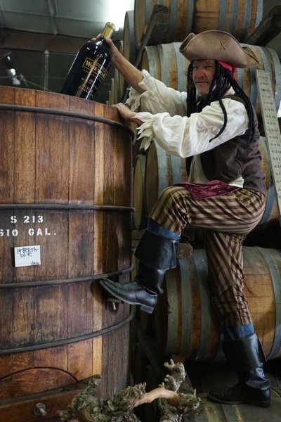 Peter Ficklin dressed as a pirate on Halloween climbing up a large, old wine cask with a bottle of Port in his hand.