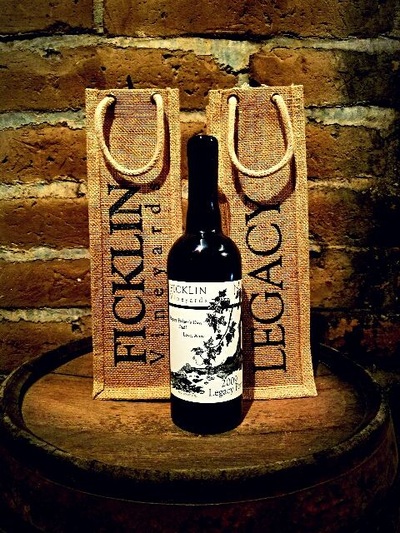 A bottle of Legacy Port flanked by 2 burlap bottle bags--one is printed Ficklin Vineyards, and the other is printed Legacy.