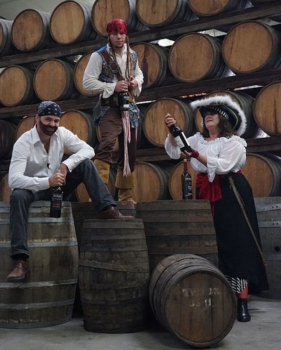 Three employees dressed as pirates on Halloween pretend to raid treasured Ficklin Ports as they stand among stacks of wine barrels.