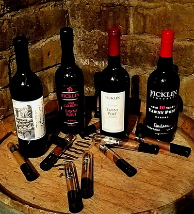 An assortment of 4 bottles of Ficklin Tawny Ports on a barrel top with an assortment of Payne Mason cigars.